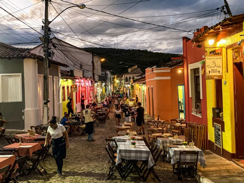 Rua de pedra do centro histórico de Lençóis à noite, com mesas de restaurante e casarios coloridos iluminados