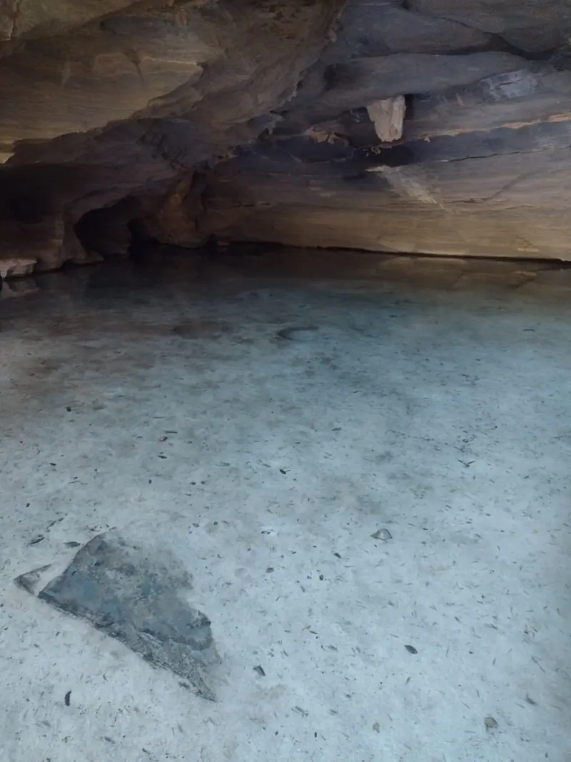 Lago de fundo arenoso claro dentro de gruta, com a rocha escura formando o teto