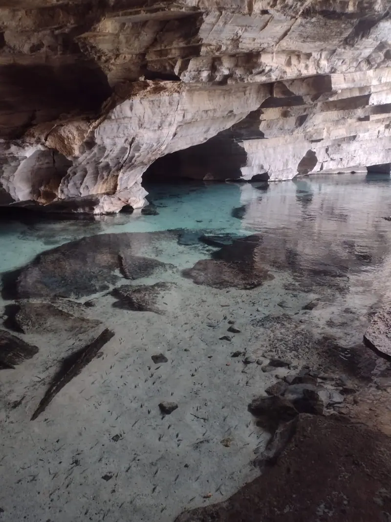 Interior de caverna com lago de água cristalina e teto de rocha estratificada na Chapada Diamantina
