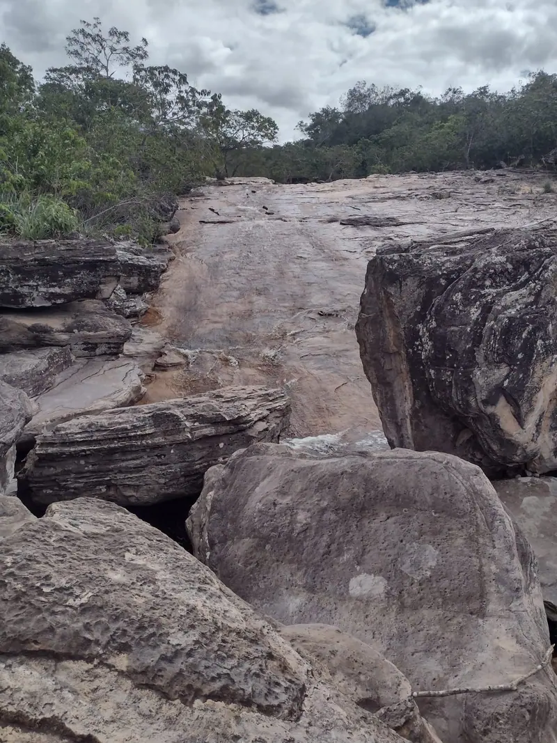 Grande lajedo de pedra lisa esculpido pela água, cercado de vegetação da Chapada Diamantina