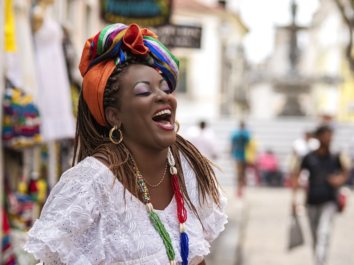 Baiana de acarajé com traje típico e turbante sorrindo em uma rua do Pelourinho, em Salvador