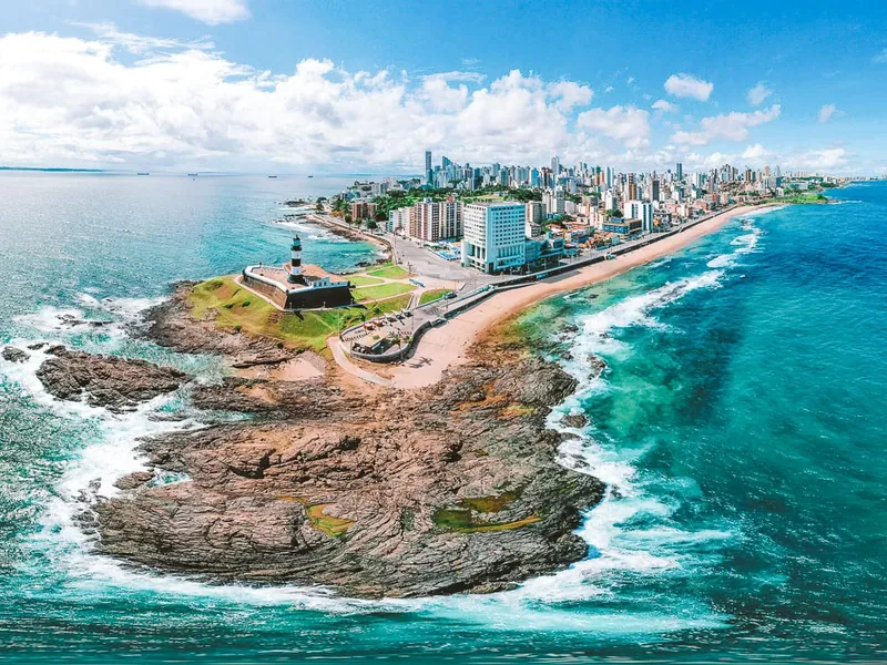 Vista aérea do Farol da Barra na ponta da península, com a orla e os prédios de Salvador ao fundo