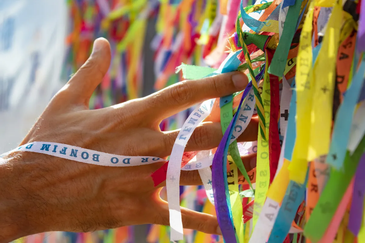 Mão amarrando fitinhas coloridas do Senhor do Bonfim nas grades da igreja, em Salvador